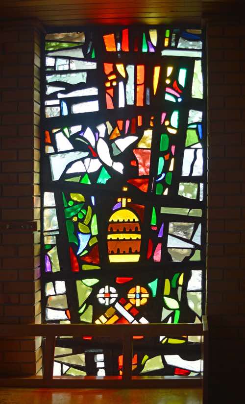 This is a rather more ‘Roman Catholic’ window in design.  At bottom are the crossed keys given to Peter (Matt 16:19).  These have since been taken as a symbol of papal authority.  Above this is a represntation of the papal tiara or crown.  And at the top is a dove and flames representing the coming of the Holy Spirit at Pentecost. 