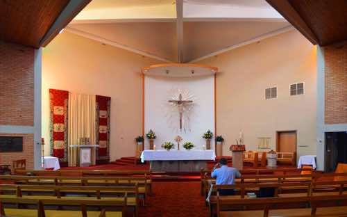 The structural lines of the sanctuary are cleverly placed to focus attention on the central crucified Christ behind the altar.  At left is the tabernacle, and at right the ambo, Paschal candle, and baptismal font.