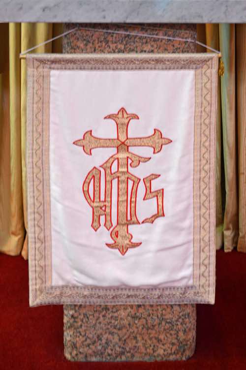 The banner below the tabernacle displays the letters ‘IHS’ which is a Christogram:  the first three letters of the name ‘Jesus’ in Latinized Greek.  This Christogram also includes a budded cross.  As the Society of Jesus, the Jesuits took the IHS as their sign.
