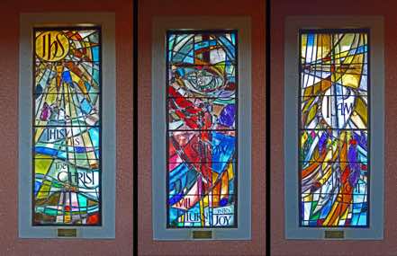 The three windows towards the East have the following text (from the left):  ‘IHS  This  is the Christ’;  ‘Sorrow will turn into Joy’; ‘I am the Light’.  These are quotes from St John’s Gospel – a reminder that this is the Cathedral of St John the Evangelist.  [Click to ZOOM.]