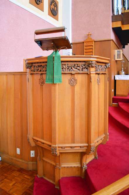At left is the pulpit, from where the Word of God is expounded each week.  The pulpit was designed by R. S. D. Hannan, and was carved by Guernsey, Christchurch.  [12]