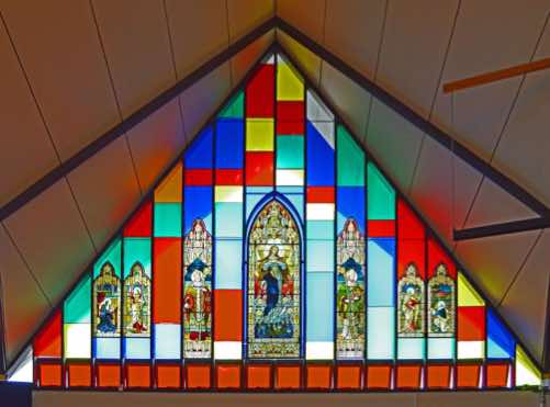 The sanctuary is surrounded by these colourful triangular windows defined by the lines of the roof.  The windows are glazed with plain coloured glass, but with stained glass inserts from the old St Mary’s.